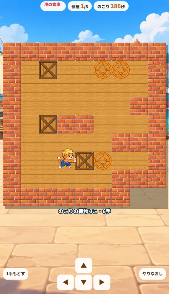 スマホの縦画面で、木の床の部屋にレンガのかべと木箱、オレンジの置き場、ねこの作業員があり、下に矢印ボタンがある場面