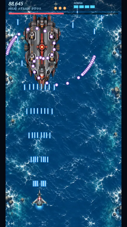 スマホの縦画面で、海の上の戦艦ボスが撃つ弾の列の下を、白銀の戦闘機がショットを撃ちながら進んでいる