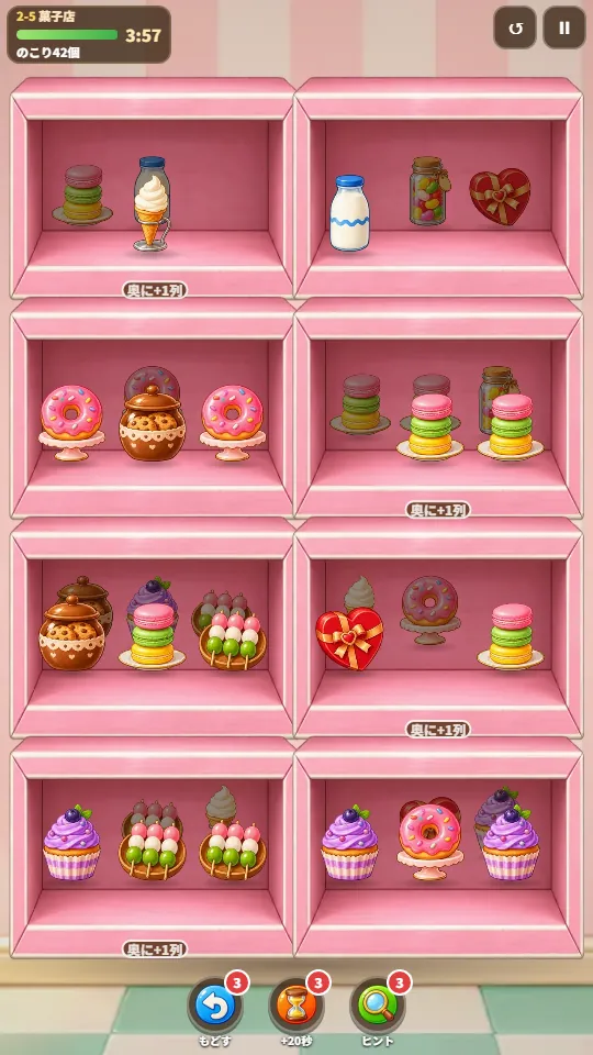 スマホの縦画面。お菓子屋さんのピンクのキューブ棚の小部屋にお菓子が並び、うしろに次の列の品物が暗く見えている。上にのこり時間のバー、下に丸いおたすけボタン